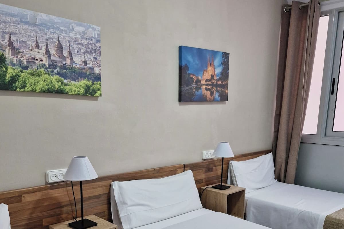A hotel room with two beds, a wooden headboard, a nightstand with a lamp, a painting of a cityscape, and a window with curtains.