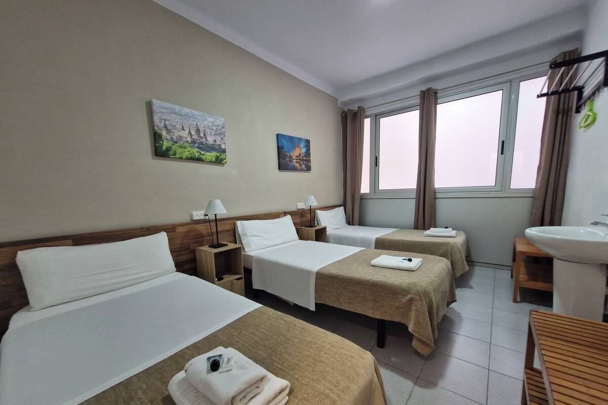 A hotel room with two beds, a small desk, a sink, and two windows with curtains.