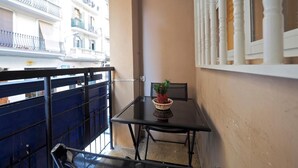 A balcony with a table and chairs, a potted plant, and a view of a building with balconies. - Hostal Elkano (Barcelona)