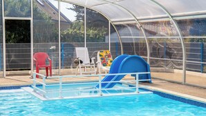 Una piscina con tobogán, cubierta por un techo transparente y rodeada de sillas y una valla.