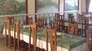 A dining area with long tables, wooden chairs, and a mural of a landscape on the wall. - Hotel Merloni (Grandola ed Uniti)