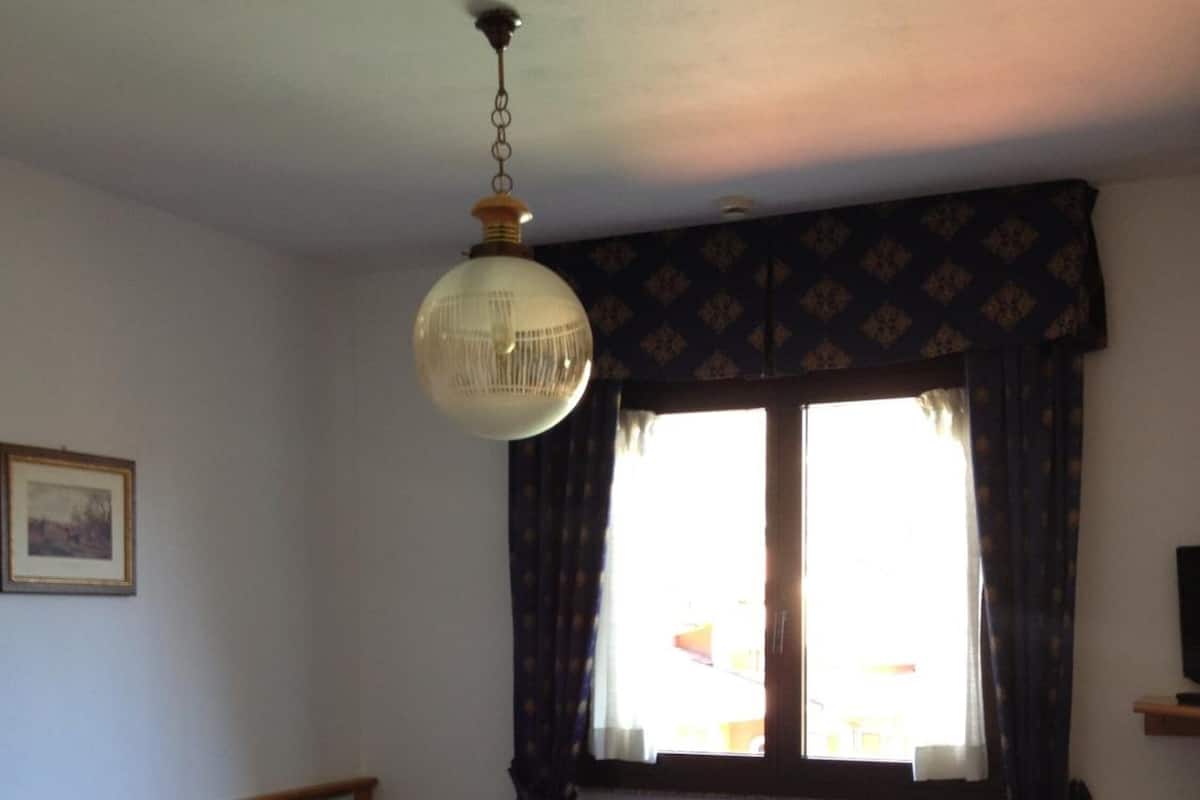 A bedroom with a bed, a ceiling fan, a window with curtains, a radiator, and a framed picture on the wall.