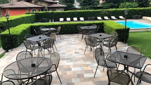 An outdoor patio with tables and chairs, a swimming pool, and a view of surrounding houses and mountains. - Hotel Merloni (Grandola ed Uniti)
