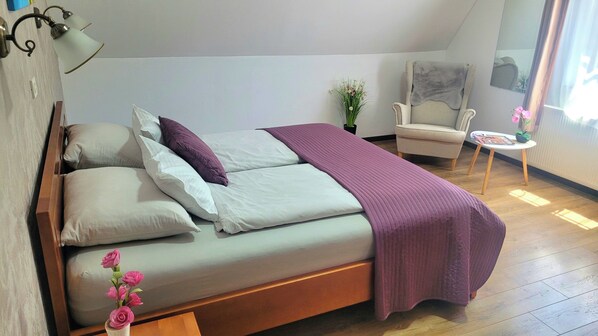 Un dormitorio con cama, una silla, una mesita y una planta en maceta.