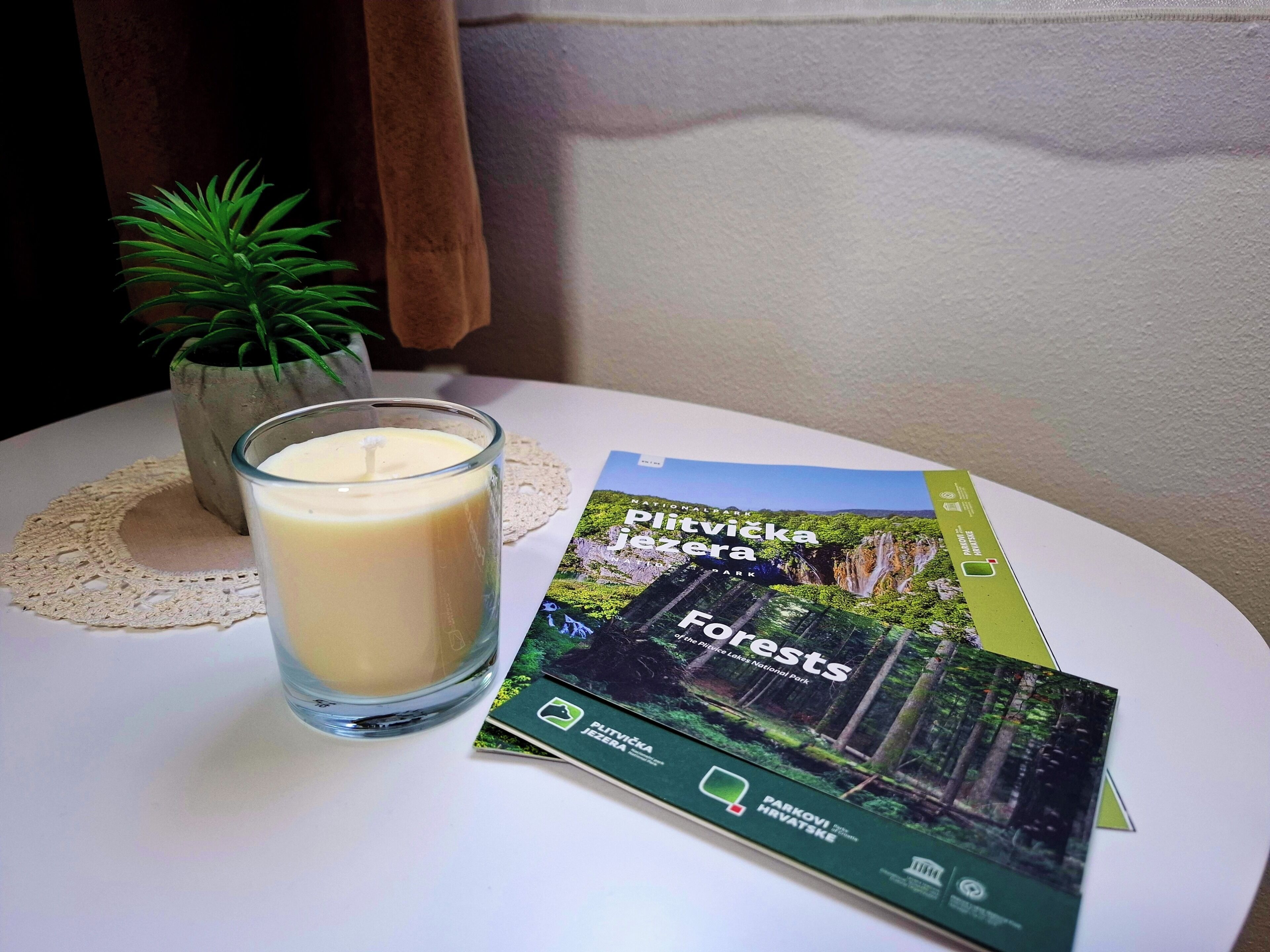 A glass candle on a table with a brochure and a small potted plant.