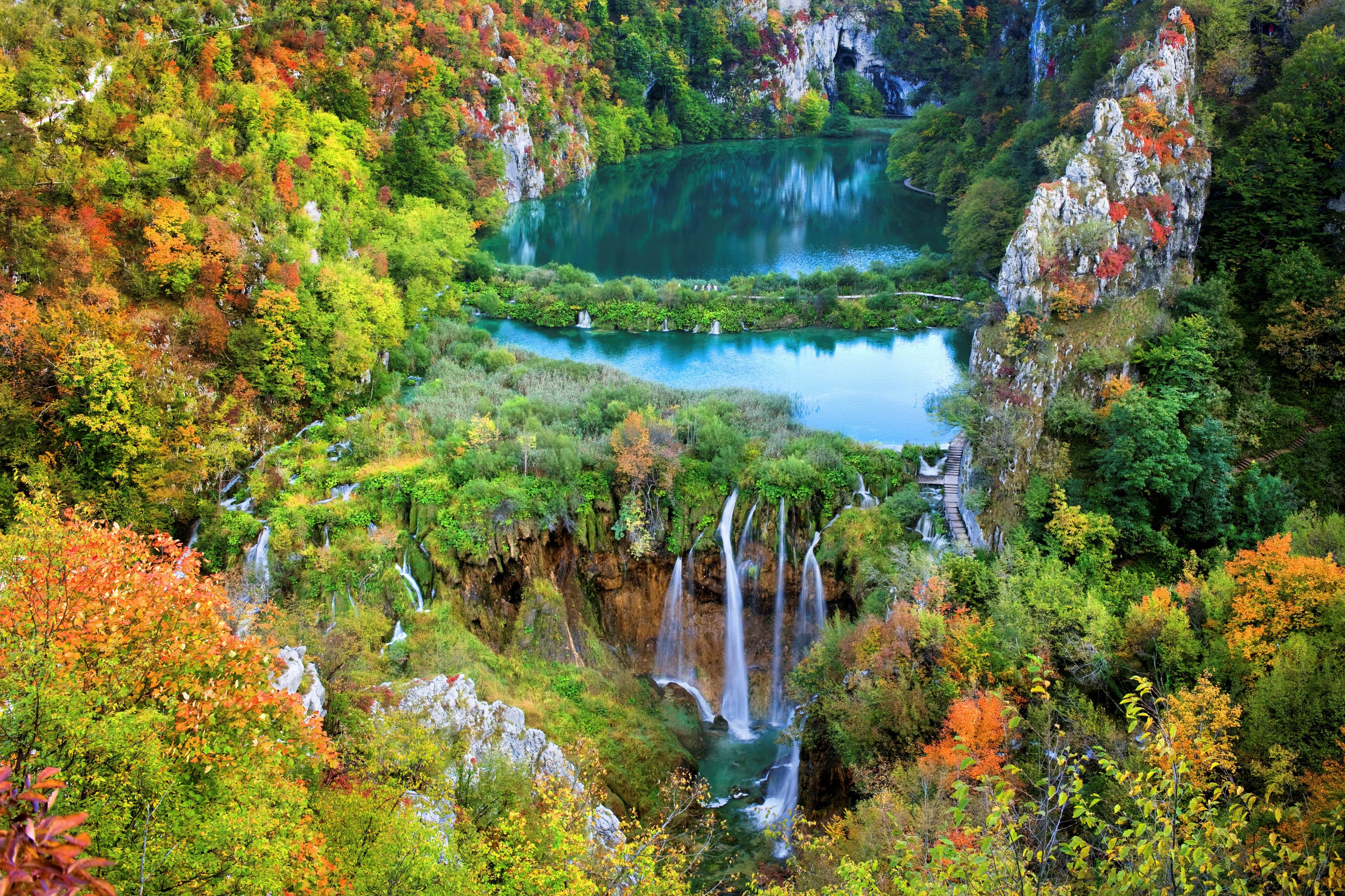 Paisaje montañoso con cascadas y un lago rodeado de árboles de colores otoñales.