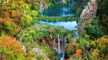 Paisaje montañoso con cascadas y un lago rodeado de árboles de colores otoñales.