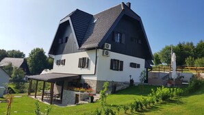Ein traditionelles Chalet mit steilem Walmdach, Stein Fundament und einer Terrasse mit Sitzgelegenheit.