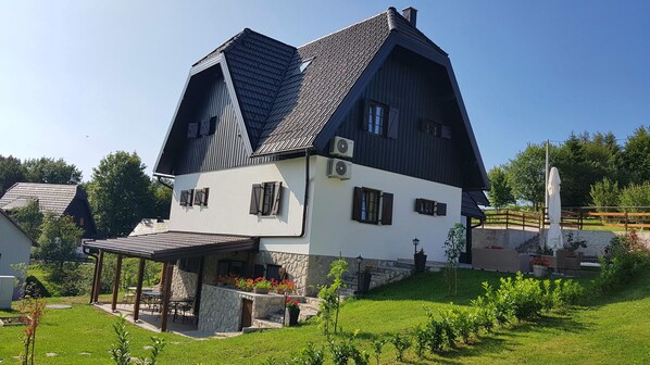 A traditional chalet with a steeply pitched roof, stone foundation, and a patio area with outdoor seating.