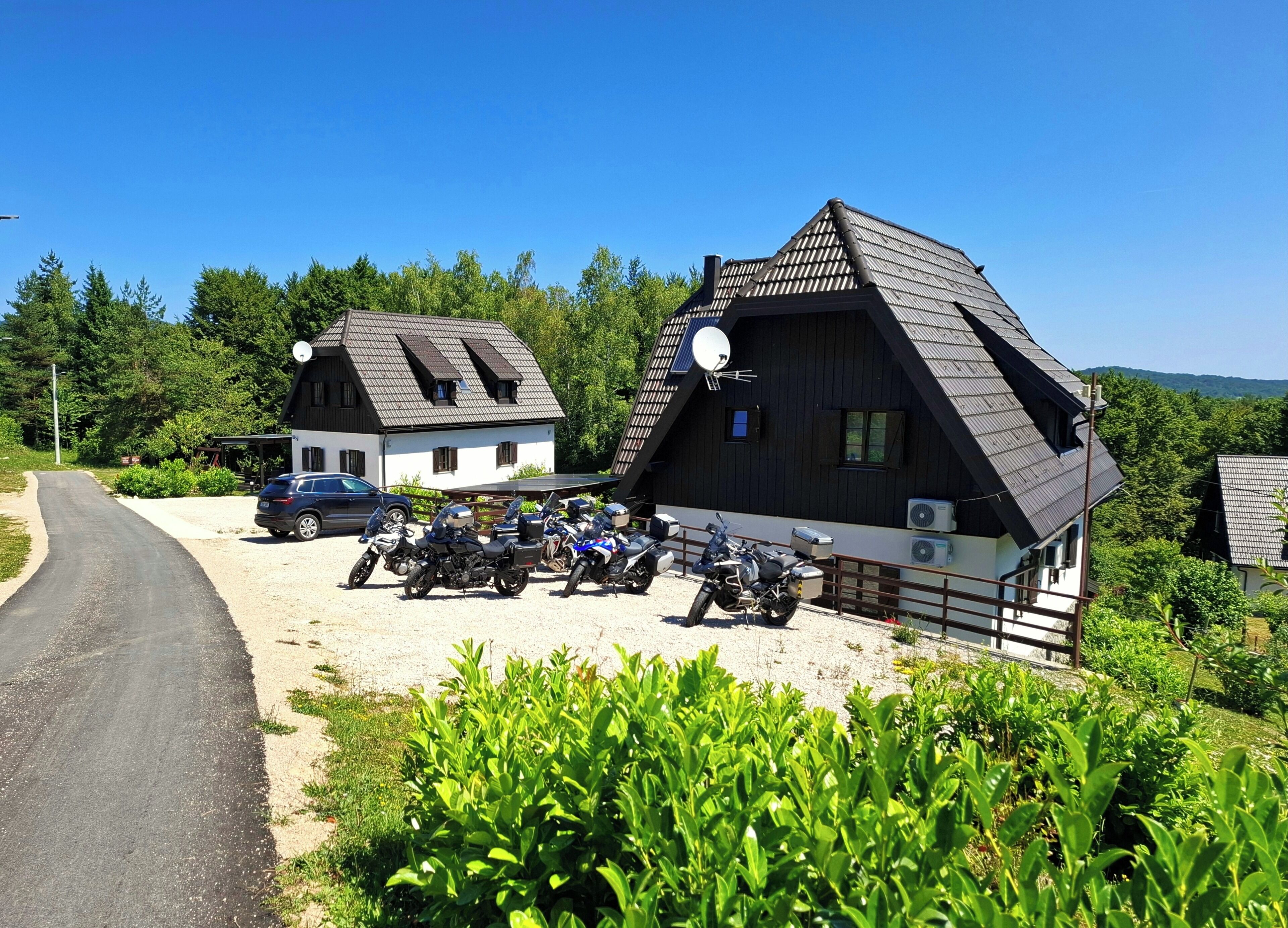 A rural setting with two houses, a gravel driveway, and several parked motorcycles.
