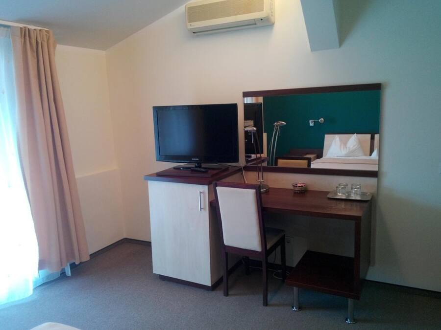 A hotel room with a desk, chair, TV, and a bed.