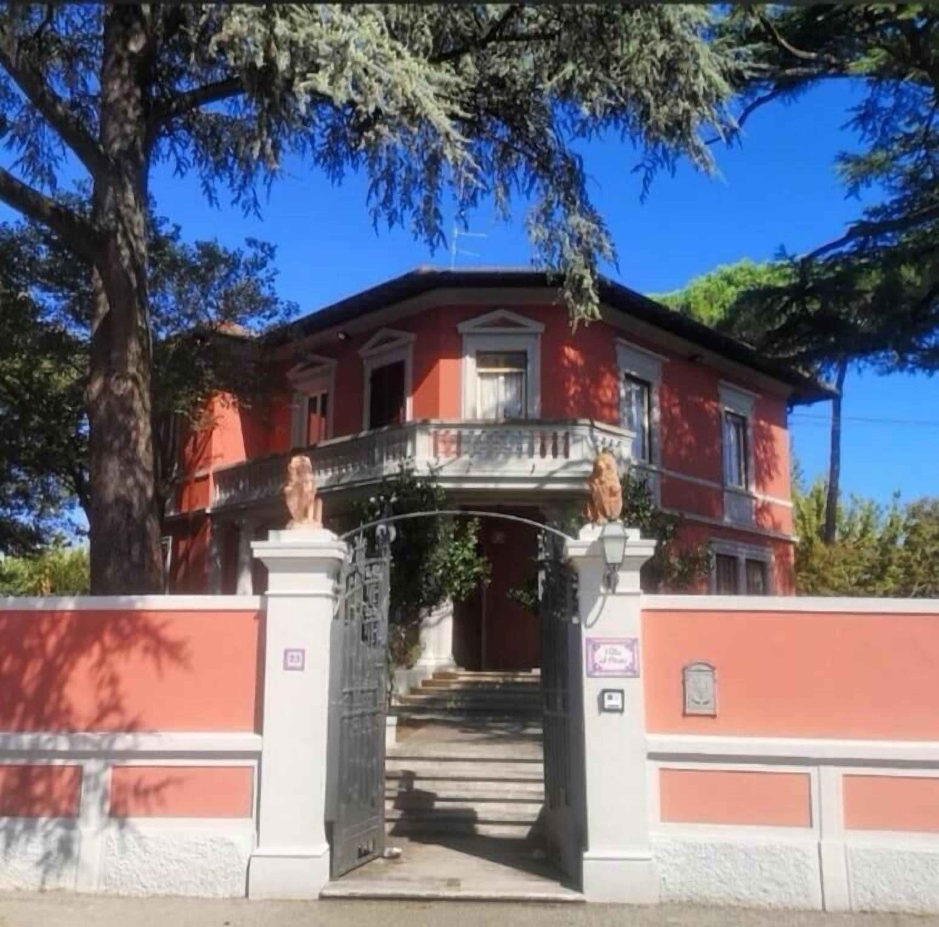 A red building with a white balcony and a statue at the entrance.