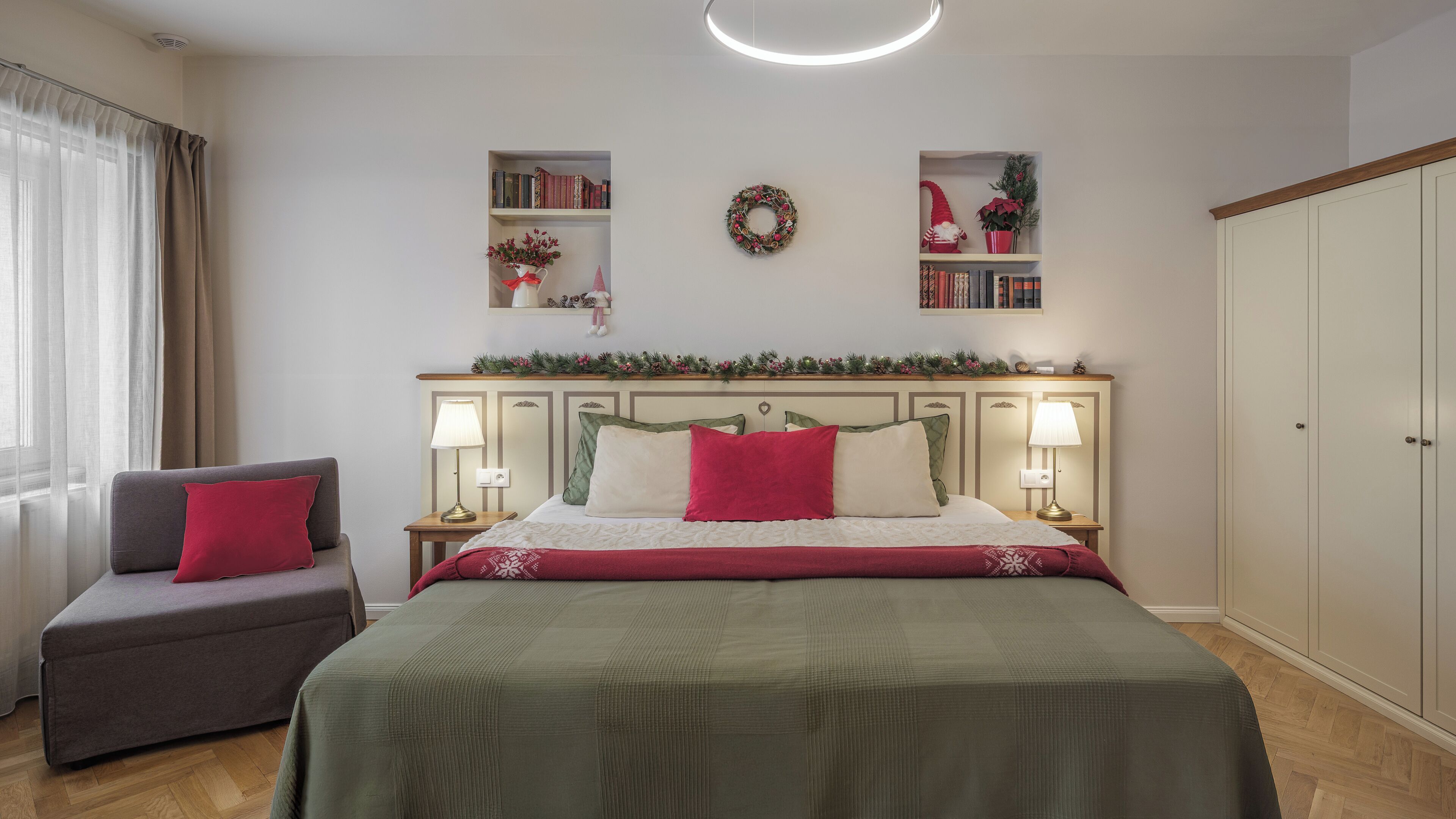 Un dormitorio con cama, dos mesitas de noche con lámparas, una silla, un armario y una estantería con libros y un adorno circular.