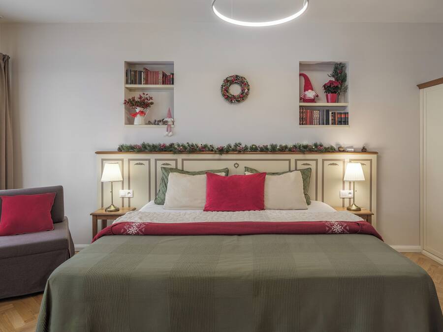 Un dormitorio con cama, dos mesitas de noche con lámparas, una silla, un armario y una estantería con libros y un adorno circular.