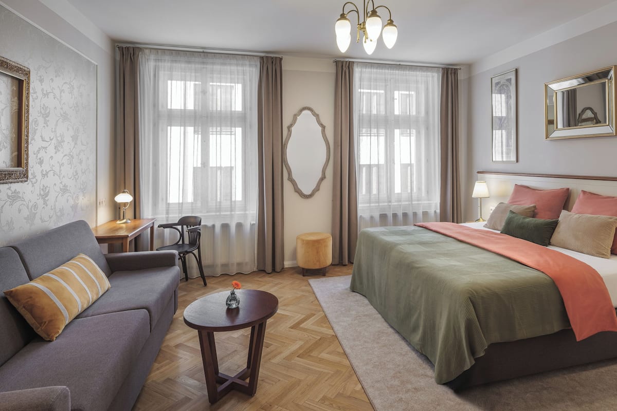 A hotel room with a bed, a sofa, a small table, a chair, and a mirror.