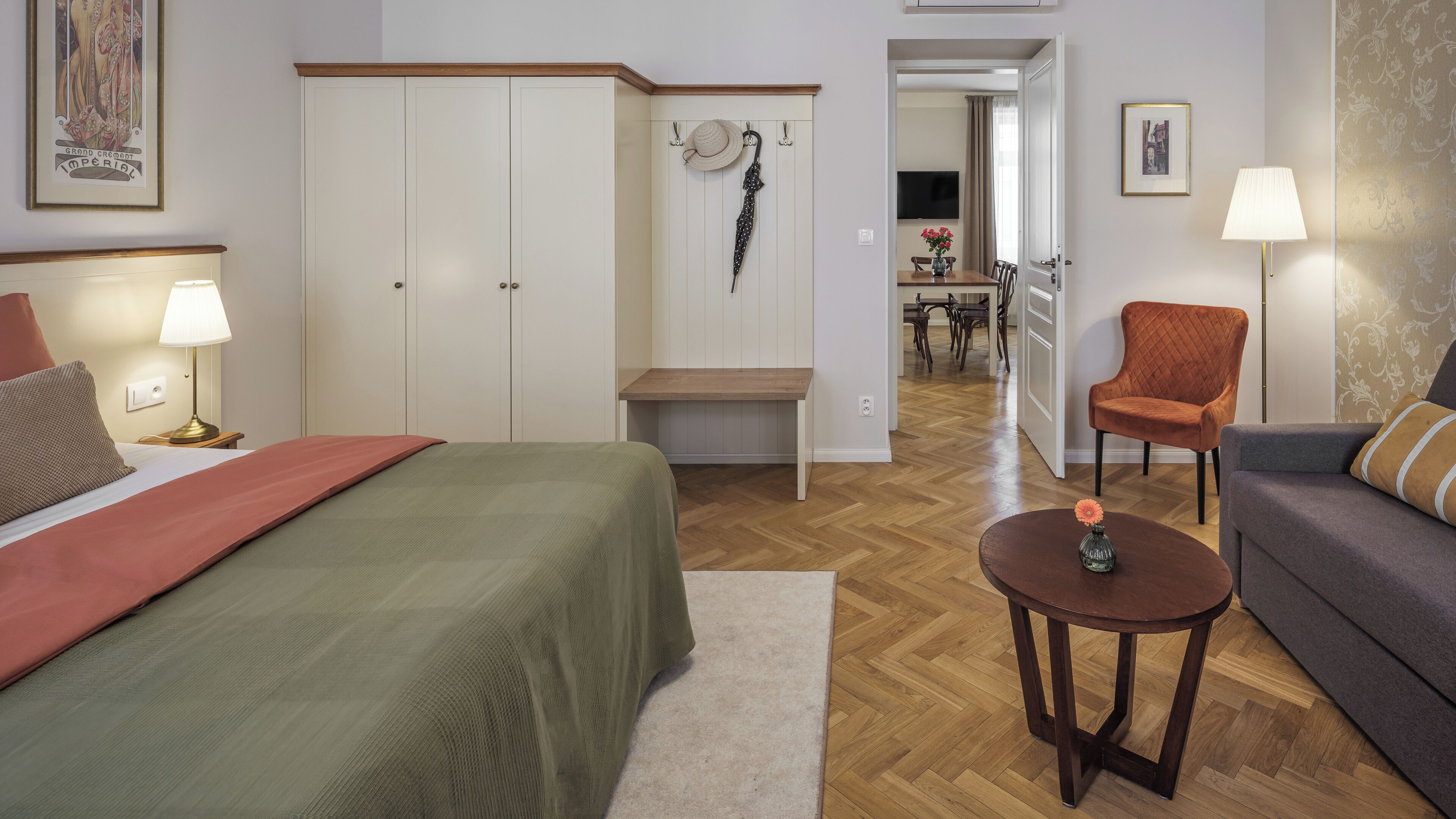 A bedroom with a bed, bedside table, lamp, and a view into the dining area.