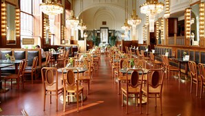 Un restaurante espacioso con techos altos, candelabros ornamentales y mobiliario de madera.