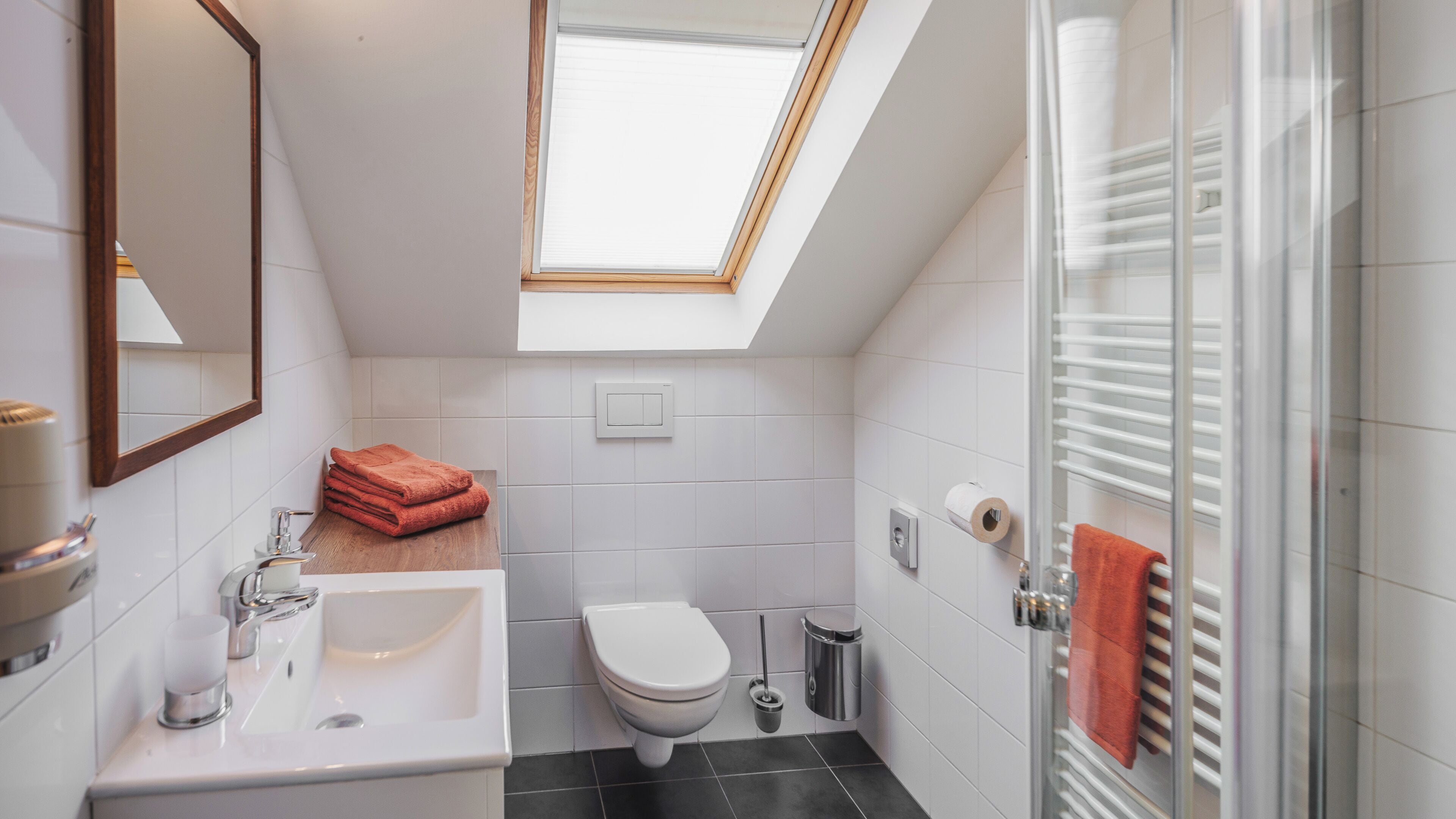 A modern bathroom with a skylight, white tiles, a white sink, a toilet, and a glass shower enclosure.