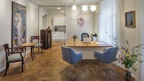 Un comedor con una mesa de madera, dos sillas azules, un jarrón con flores y un cuadro grande en la pared.