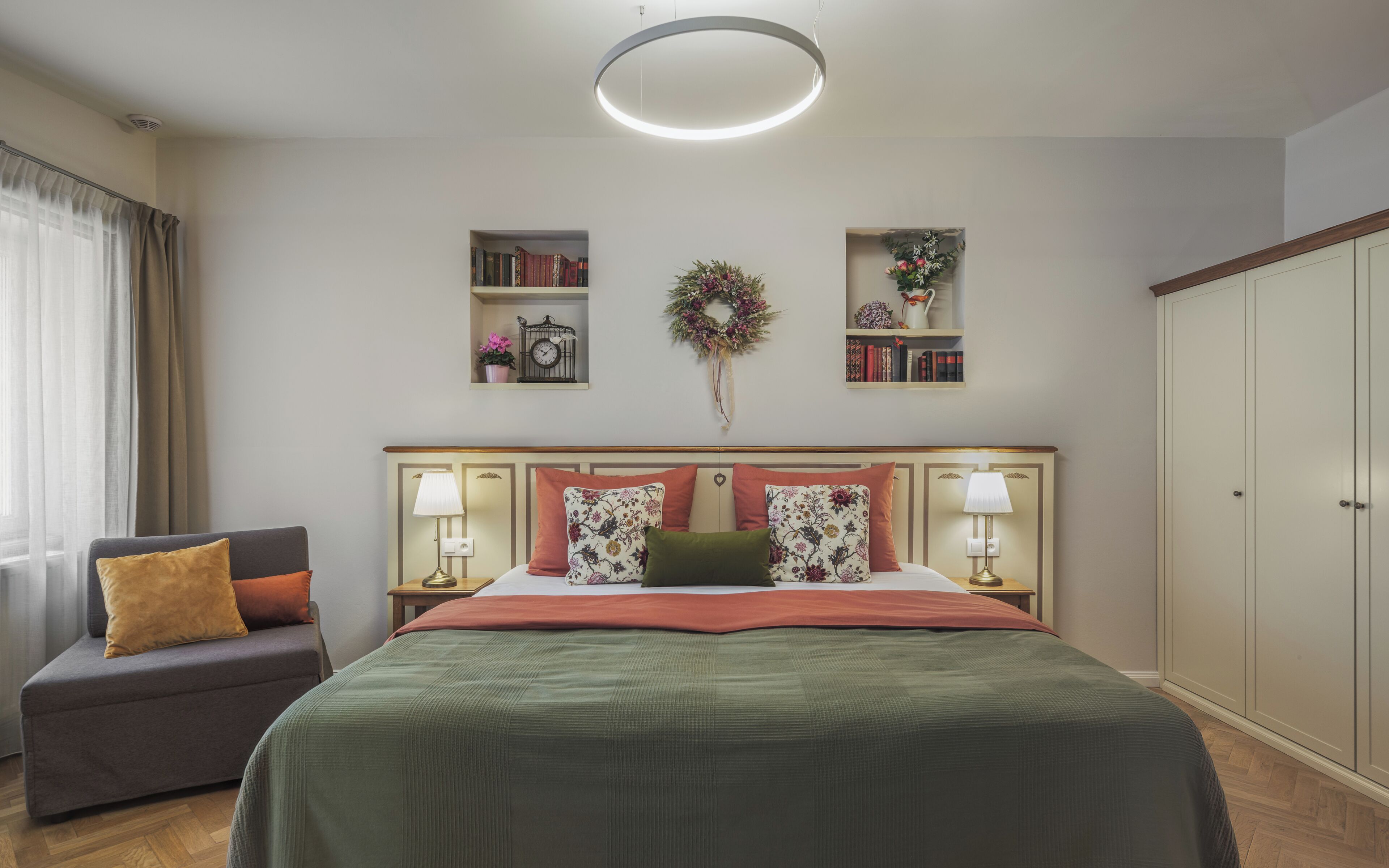 Una habitación de hotel con cama, una silla, una estantería, un armario y una lámpara en el techo.