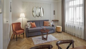 Una sala de estar con un sofá gris, dos sillones, una mesita redonda, una lámpara y un espejo en la pared.