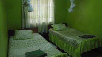 Una habitación con dos camas, cada una con colcha verde y almohadas blancas. Hay una ventana con cortinas y una mosquitera colgada.