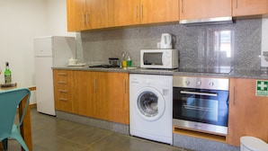 A compact kitchen with wooden cabinets, a washing machine, a microwave, and an oven. - Five Design Rooftop by Storytellers (Funchal)
