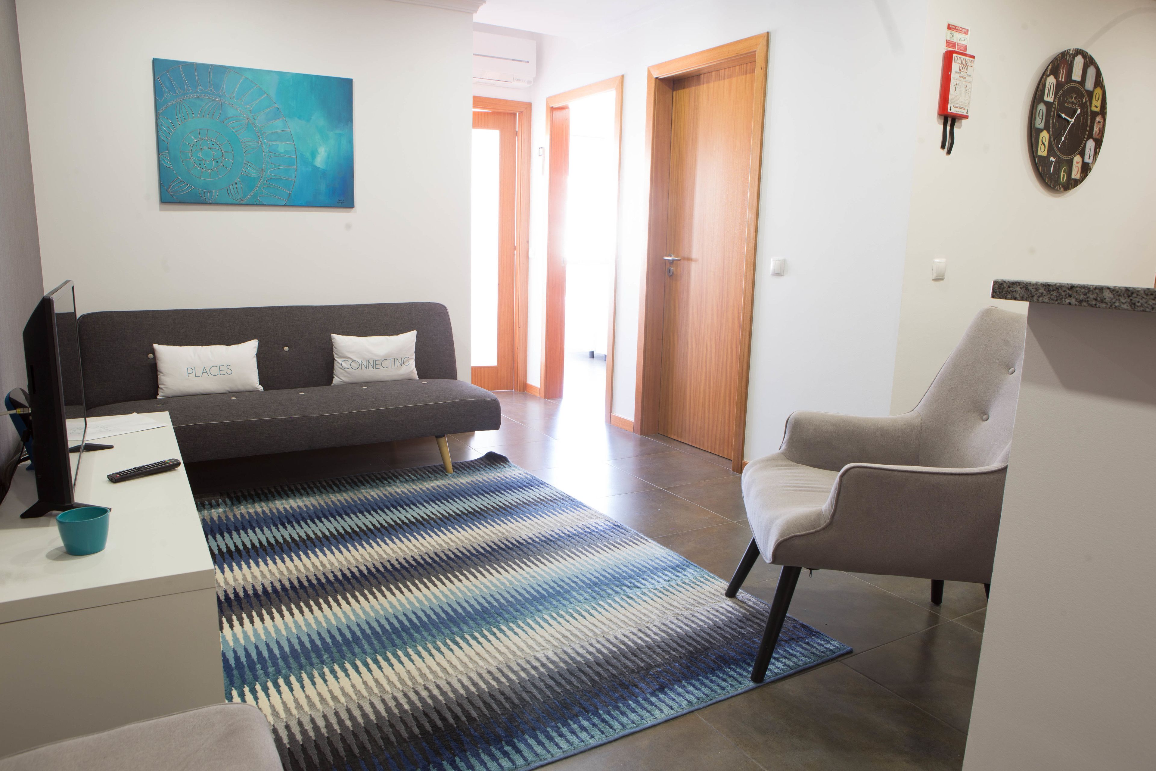 A modern living room with a sofa, a chair, a rug, a painting, and a clock on the wall.