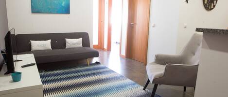 A modern living room with a sofa, a chair, a rug, a painting, and a clock on the wall.