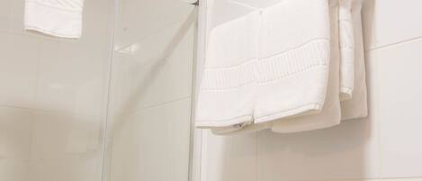 A bathroom with white tiled walls, a glass shower enclosure, and two white towels hanging on a metal towel rack.