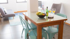 A dining area with a table set for two, featuring a bowl of fruit, a bottle of water, and two glasses of a yellow beverage. - Five Design Rooftop by Storytellers (Funchal)