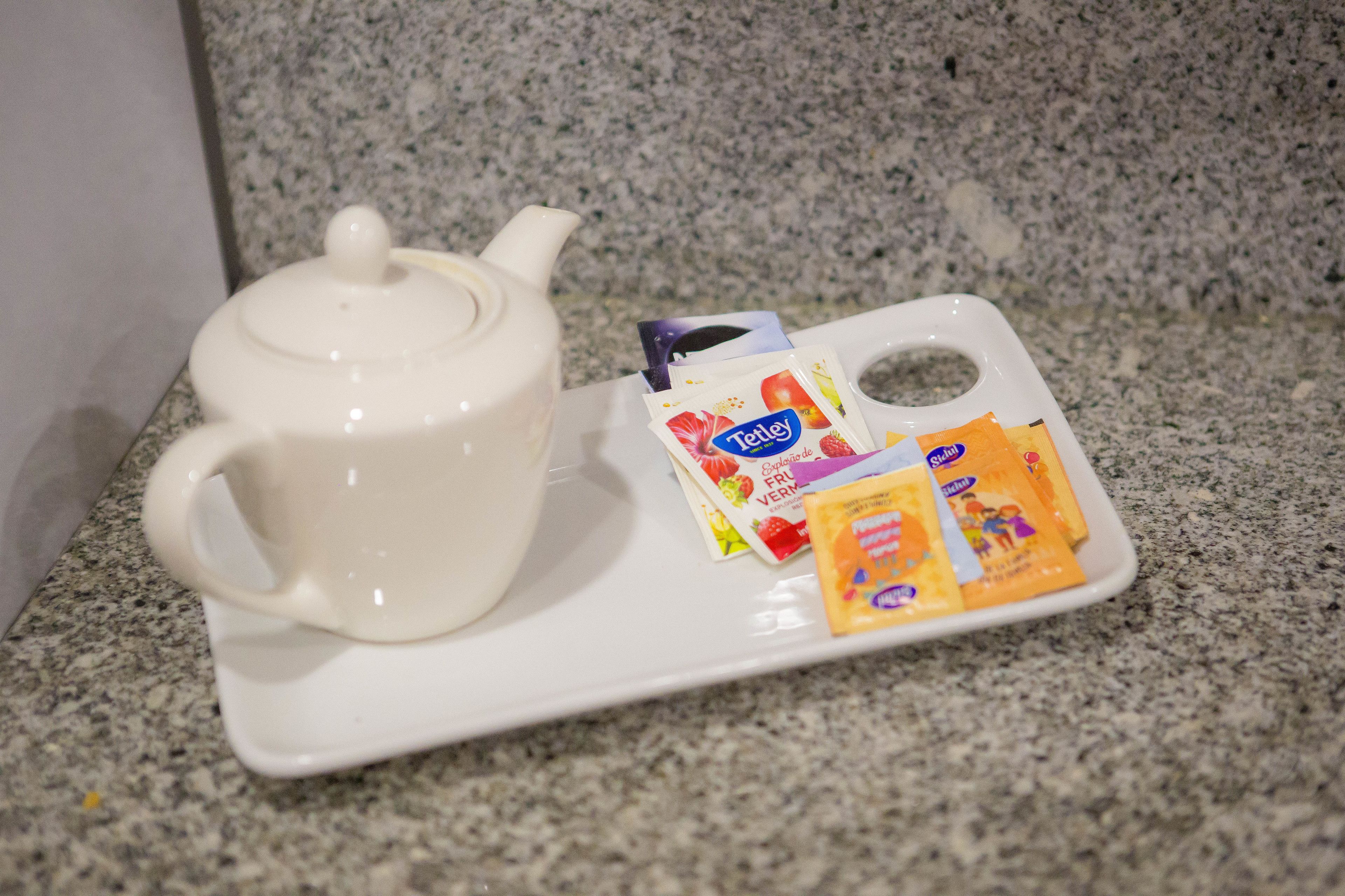 Una tetera blanca sobre una bandeja con una caja de té Tetley y un sobre de azúcar.