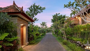 A pathway leading to a traditional building with a tiled roof, surrounded by lush greenery and a stone wall. - Bali Paradise Heritage by Prabhu (Ungasan)