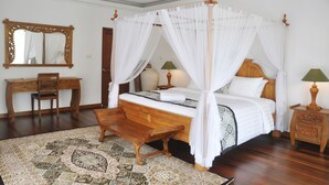 A four-poster canopy bed with a wooden bench, a desk, and two bedside lamps. - Bali Paradise Heritage by Prabhu (Ungasan)