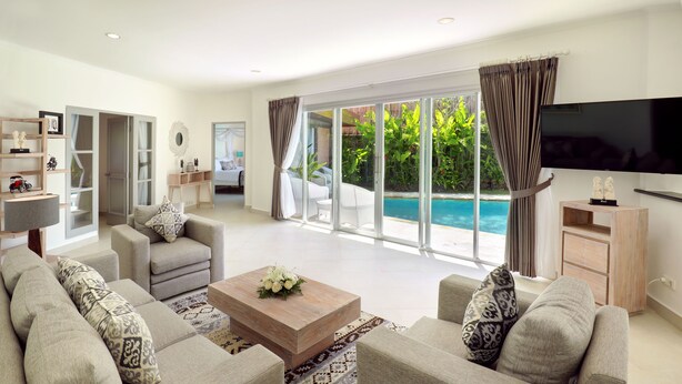 A spacious living room with a large sofa set, a coffee table, and a flat-screen TV. There is a sliding glass door leading to a pool area. - Bali Paradise Heritage by Prabhu (Ungasan)