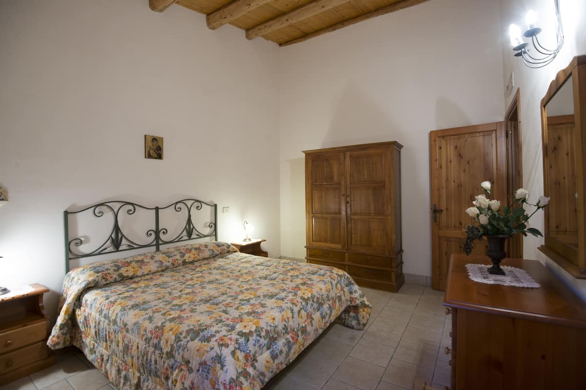 Une chambre à coucher comprenant un lit, une armoire en bois, une table de chevet et un miroir.