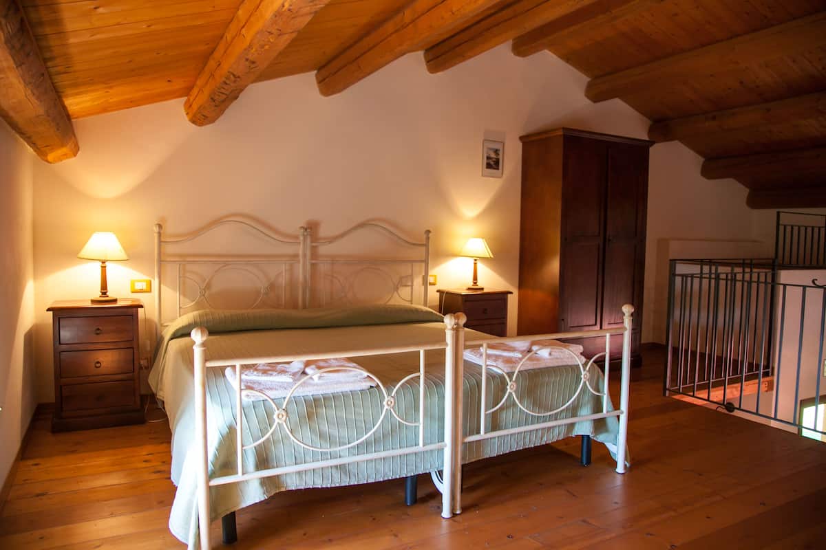 Une chambre avec un plafond en bois, un cadre de lit en métal, deux tables de chevet avec des lampes, une armoire en bois et une vue sur un balcon.