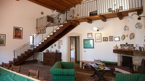 A spacious living area with a wooden staircase, a fireplace, and a dining table. - Agriturismo Borgo degli Ulivi (Palazzolo Acreide)