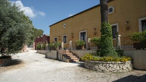 A building with a gravel driveway leading to a set of stairs, surrounded by greenery and stone walls. - Agriturismo Borgo degli Ulivi (Palazzolo Acreide)