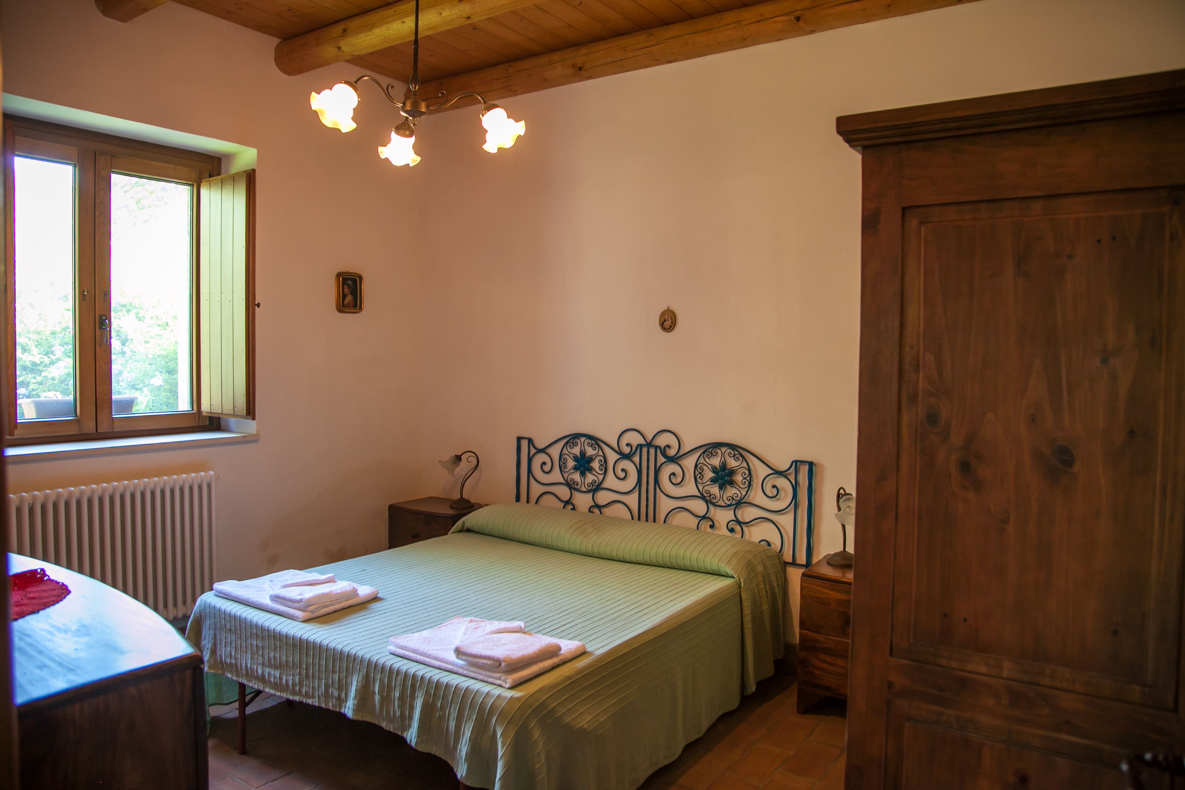 Un dormitorio con cama, cabecero de madera, mesitas de noche, un radiador y una ventana.