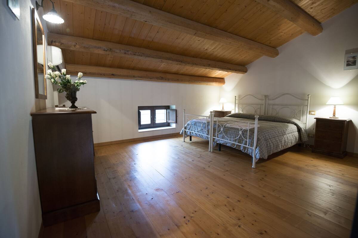 Une chambre avec un plafond en bois, un lit avec un cadre en métal, une table de chevet avec une lampe et une fenêtre donnant sur l’extérieur.