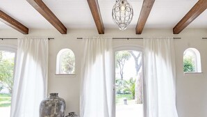Una habitación con ventanas amplias, cortinas blancas y dos jarrones en el suelo.