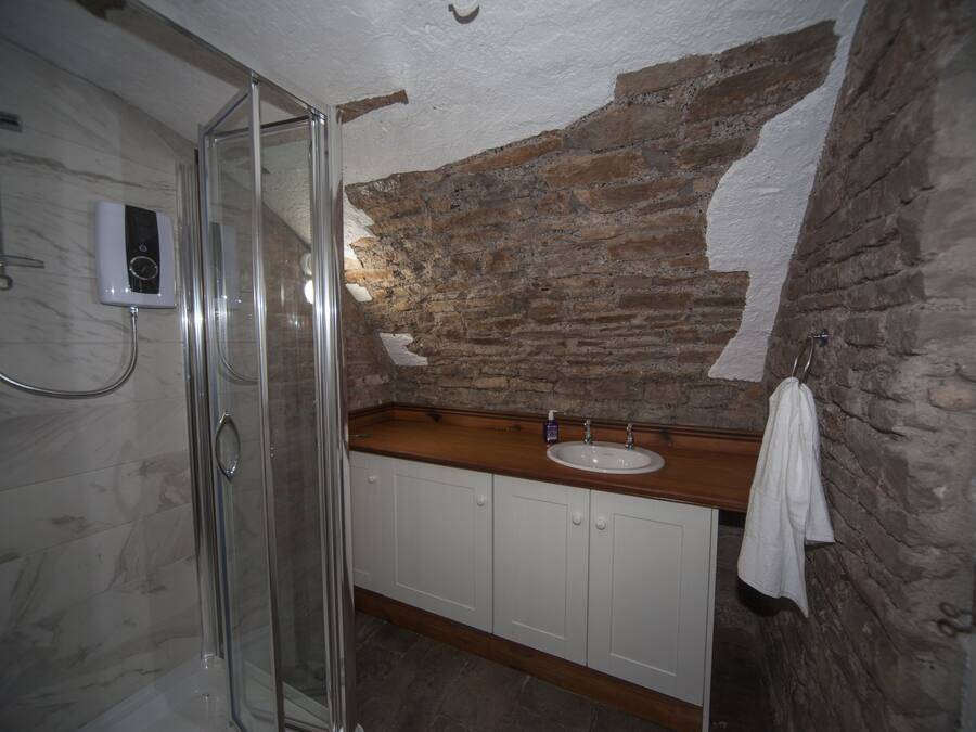 A bathroom with a glass shower enclosure, a white sink, and a wooden countertop.