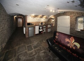 Una cocina compacta con refrigerador, microondas y cafetera. En la sala de estar, un sofá de cuero negro y un cojín estampado.