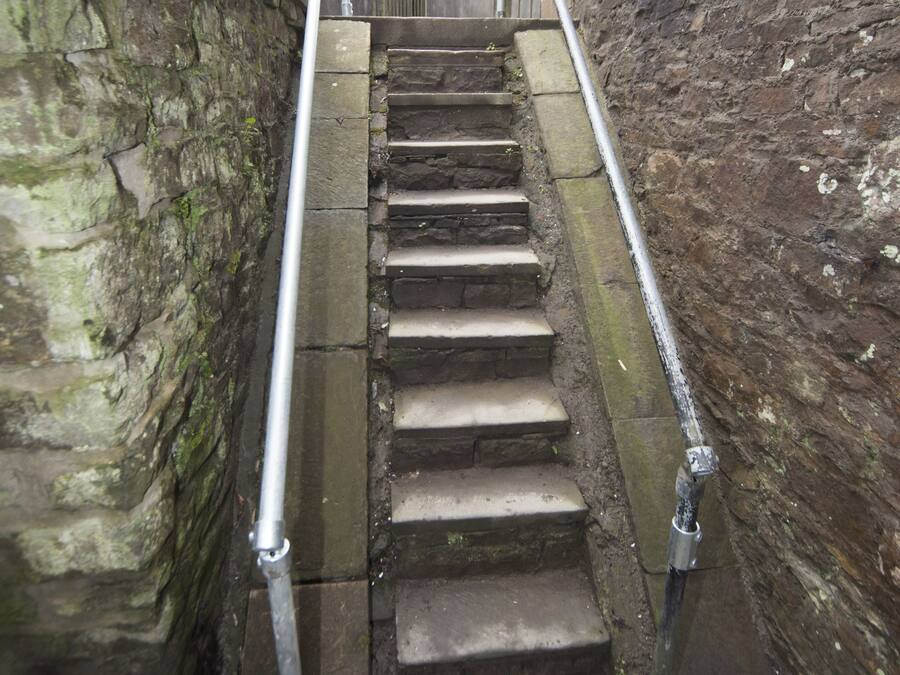 Une série de marches en pierre, dotées de rampes métalliques, menant à un escalier.