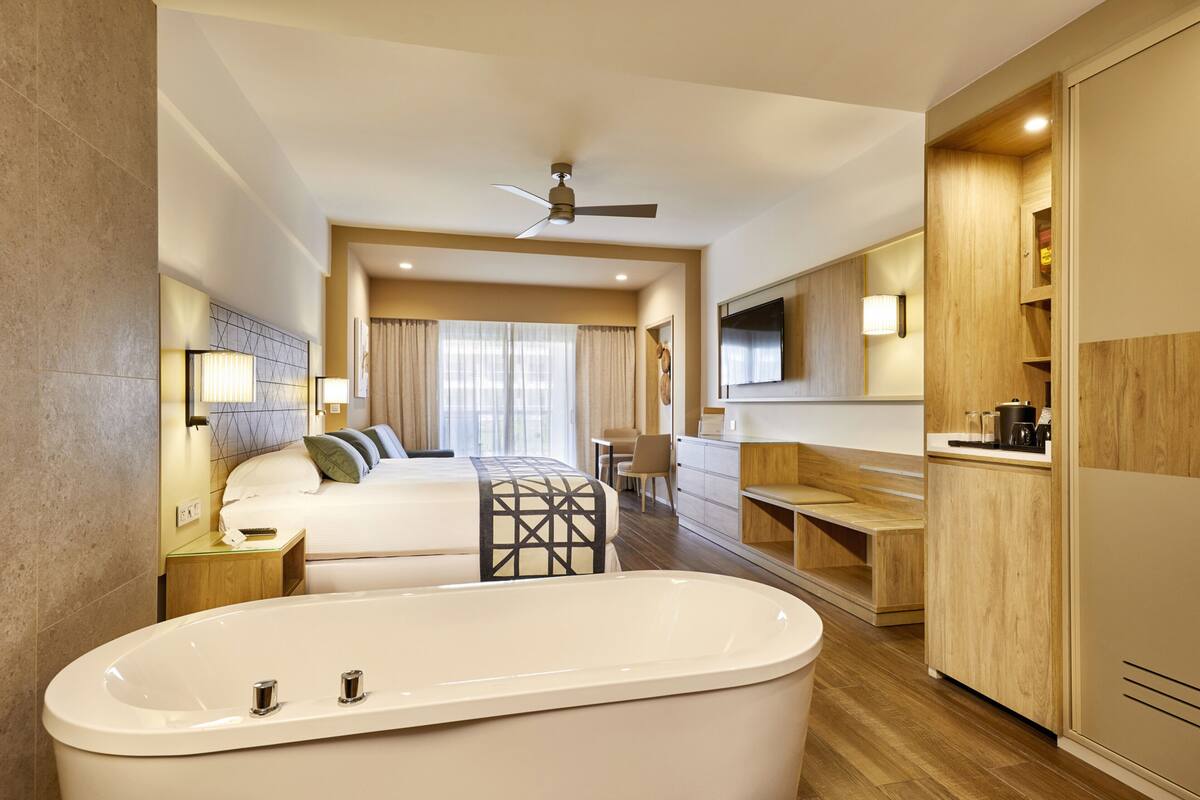 Une chambre d’hôtel moderne équipée d’une grande baignoire, d’un lit, d’un bureau et d’une télévision.