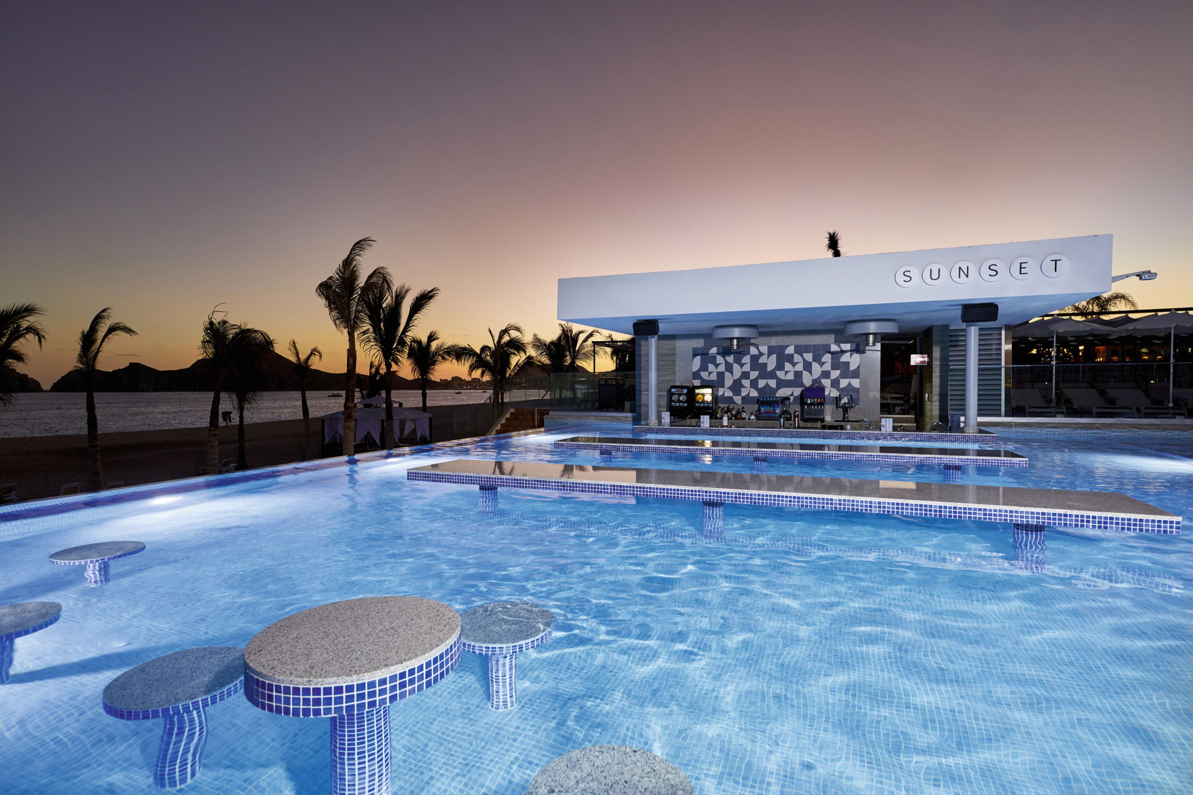 A pool area with a bar named 'SUNSET' and a sunset view.