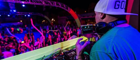 A DJ performing at a crowded event with a visible stage and audience.