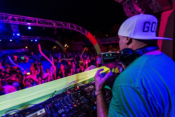 A DJ performing at a crowded event with a visible stage and audience.