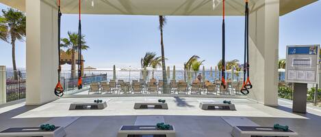A covered outdoor area with exercise equipment, seating, and a view of the ocean.